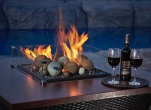 A lit table top Fire Pit with Wind Guard, a bottle of wine and two full glasses on a tray