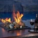 A lit table top Fire Pit with Wind Guard, a bottle of wine and two full glasses on a tray