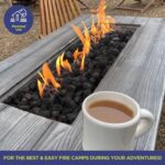 A lit Linear Gas Fire Pit with a cup of coffee in a campground