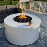 The Unity Powder Coated Metal Fire Pit 24 Inches High in White in a backyard setting